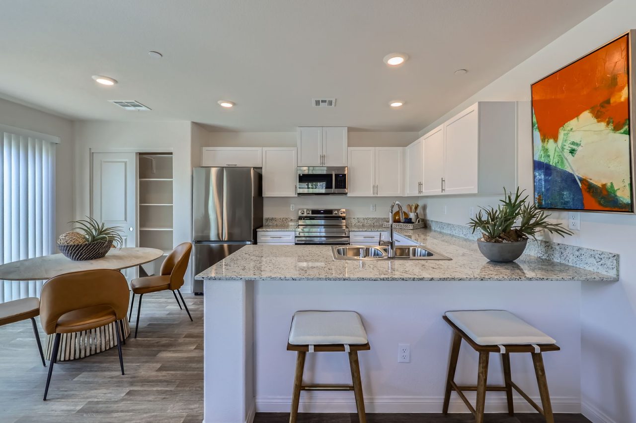 Modern kitchen featuring white cabinetry, granite countertops, stainless steel appliances, and an adjoining dining area in a Touchstone Living home.