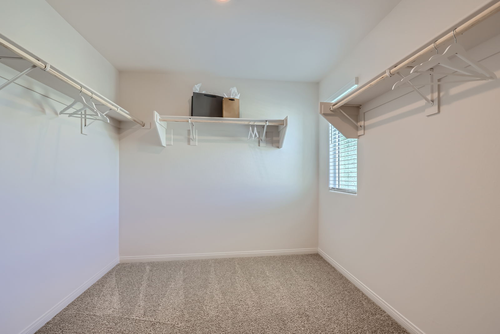Expansive walk-in closet featuring built-in white shelving, clothing rods, and plush carpeting in a Prosperity model home.