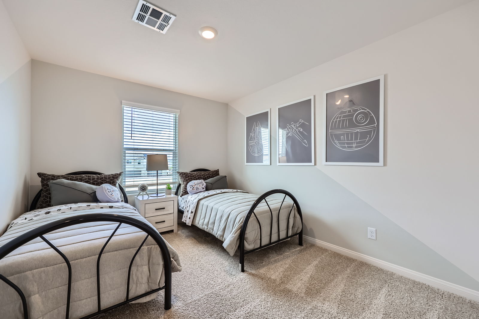Secondary bedroom staged with two twin beds, dark metal frames, and Star Wars themed artwork in a Prosperity model home.