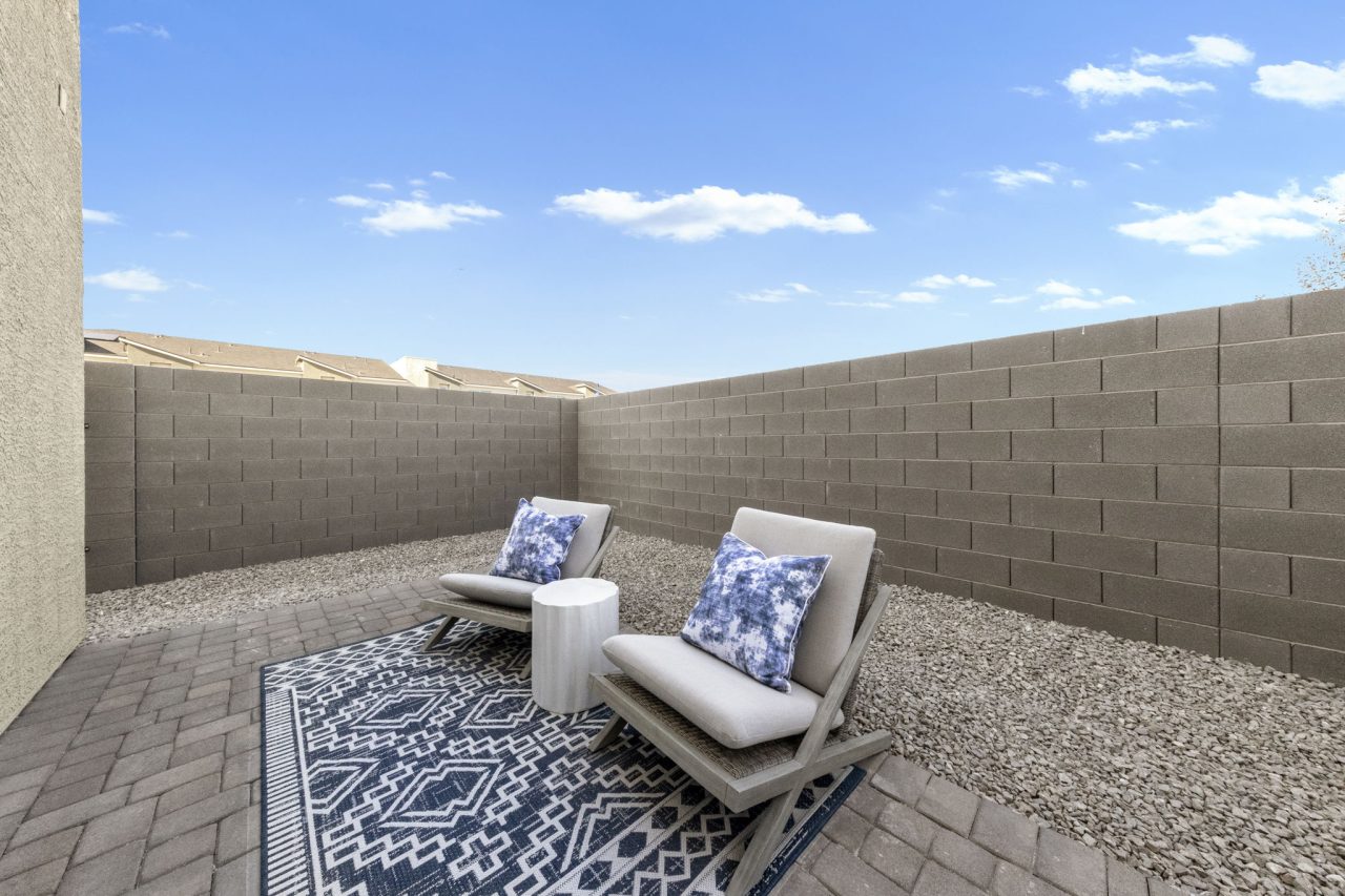 Private outdoor patio featuring brick pavers, gravel landscaping, and comfortable seating with blue patterned pillows, enclosed by a block wall at a Touchstone Living planned community.
