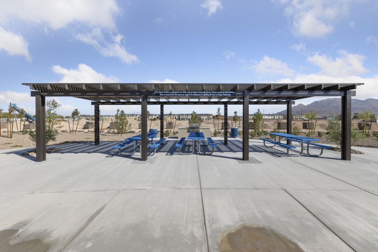 Large outdoor picnic pavilion featuring blue tables and benches under a dark metal shade structure at Independence planned community in East Las Vegas.