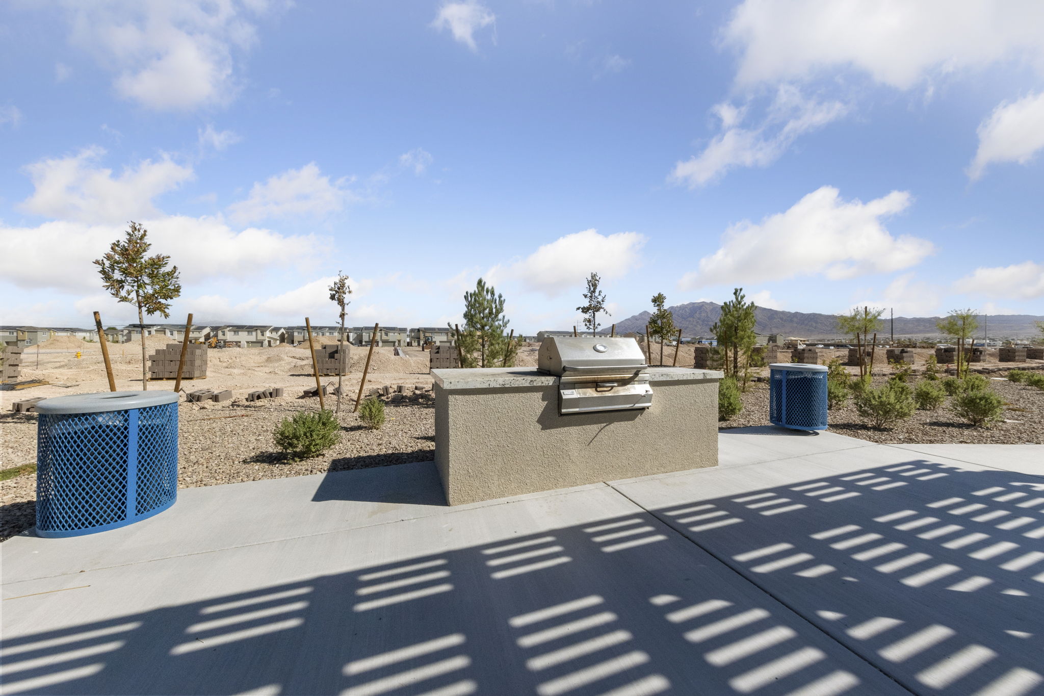 Community outdoor built-in barbecue station with a concrete countertop and blue trash cans under a shaded structure at Independence planned community.