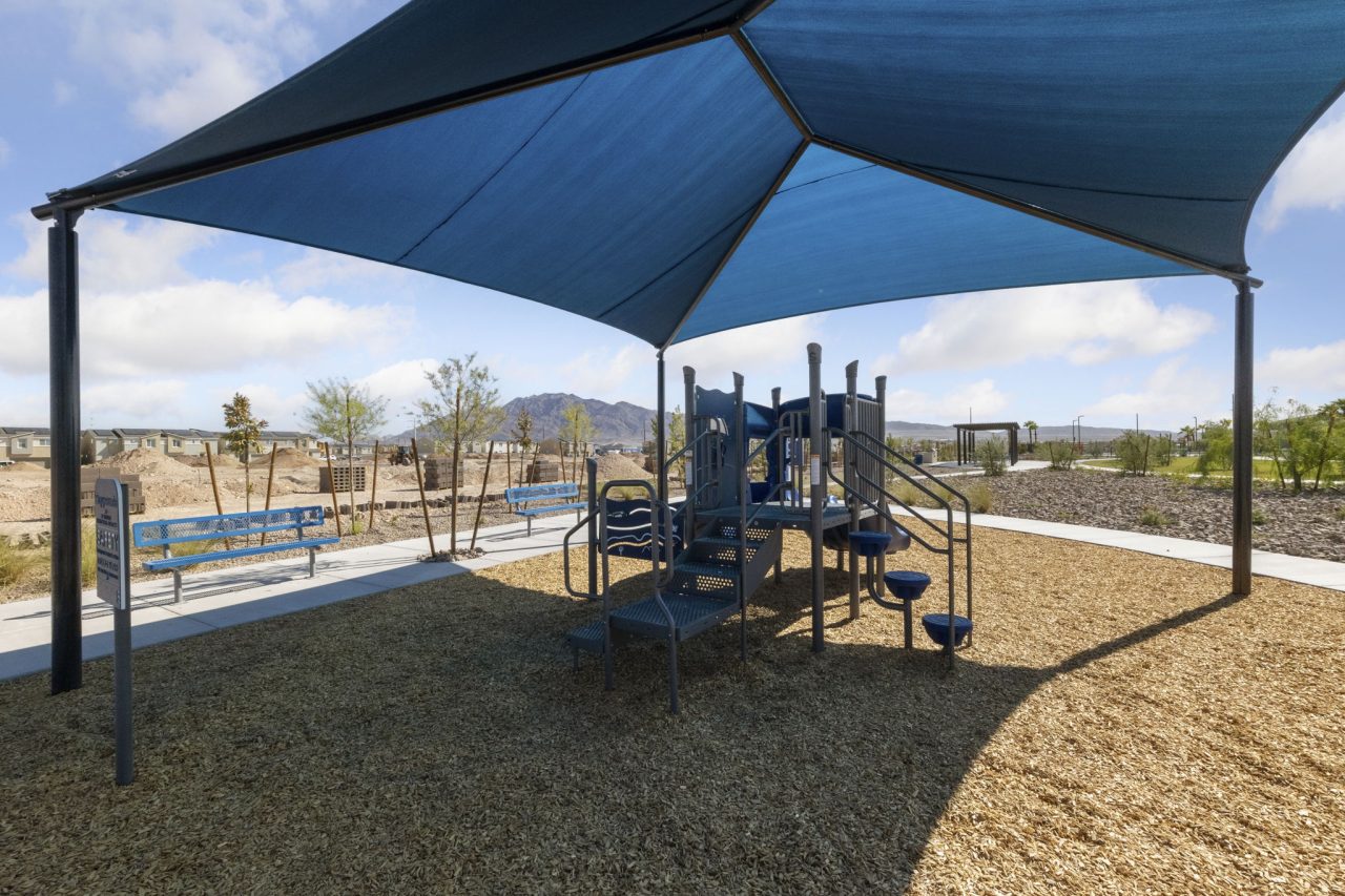 Modern children’s playground featuring climbing structures and a large blue shade structure on a bark surface at Independence planned community.