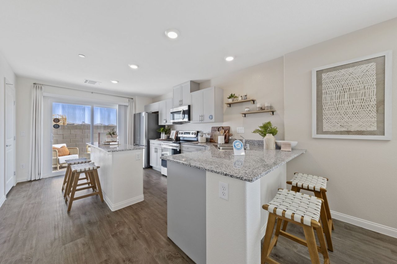 Modern kitchen featuring light grey cabinetry, granite countertops, upgraded vinyl flooring, and stainless steel Samsung® appliances in a Solaris model home.
