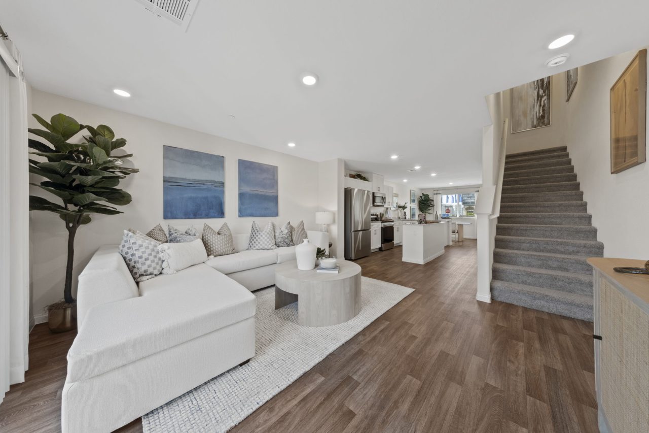 Expansive open-concept living room and kitchen featuring upgraded vinyl flooring, a white sectional, and stainless steel Samsung® appliances in a Solaris model home.