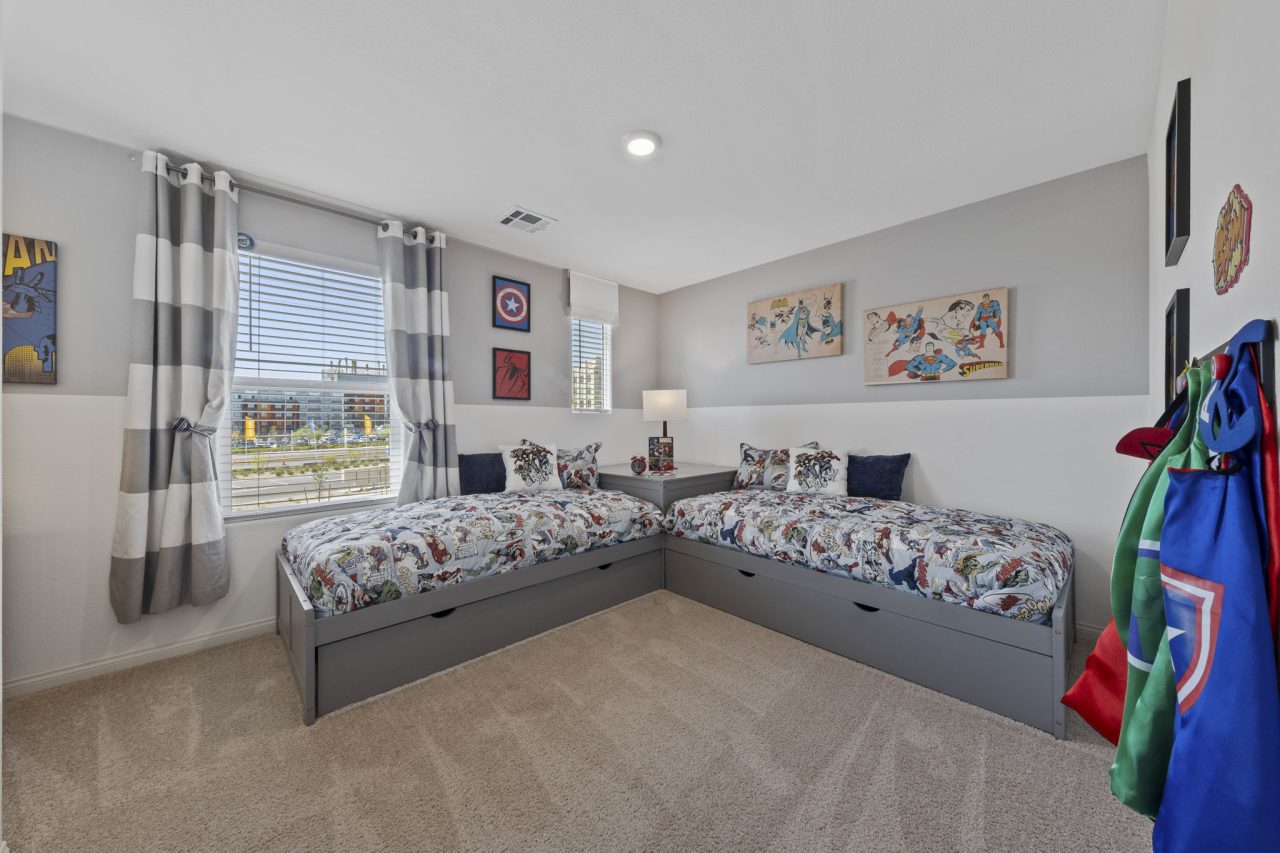 Superhero-themed kids bedroom featuring two corner-aligned twin beds with storage drawers in a Solaris model home.