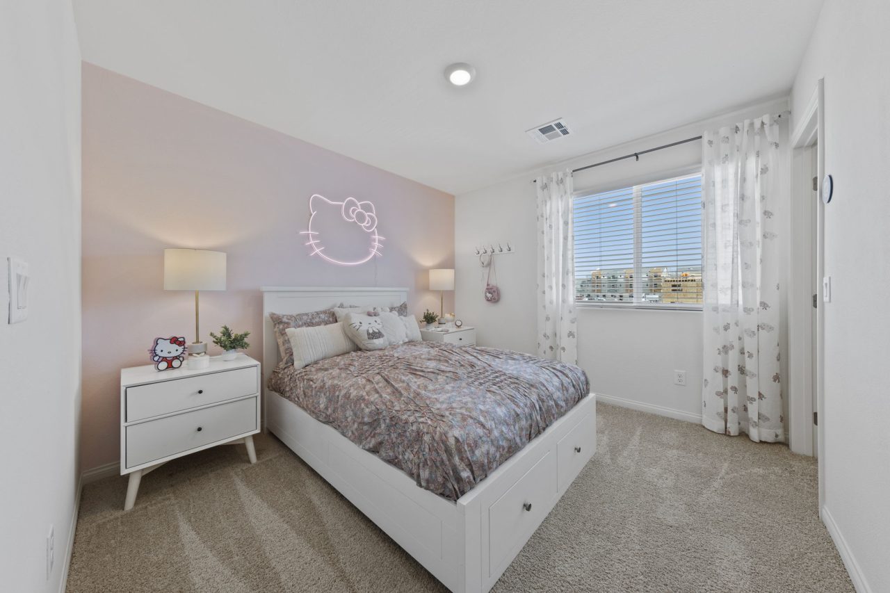 Hello Kitty-themed secondary bedroom featuring a pink accent wall, a neon sign, and a white bed with storage drawers in a Solaris model home.