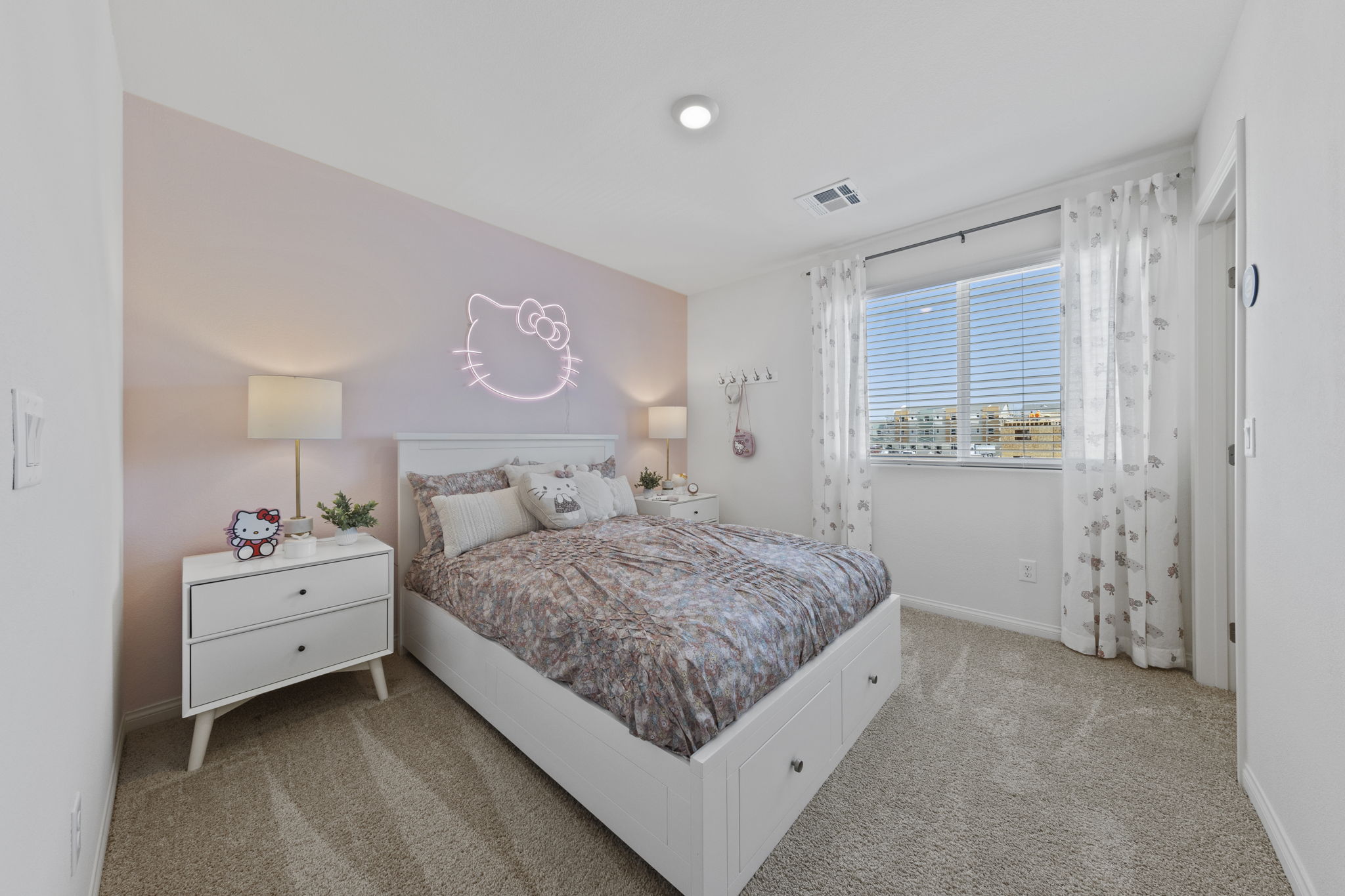Hello Kitty-themed secondary bedroom featuring a pink accent wall, a neon sign, and a white bed with storage drawers in a Solaris model home.