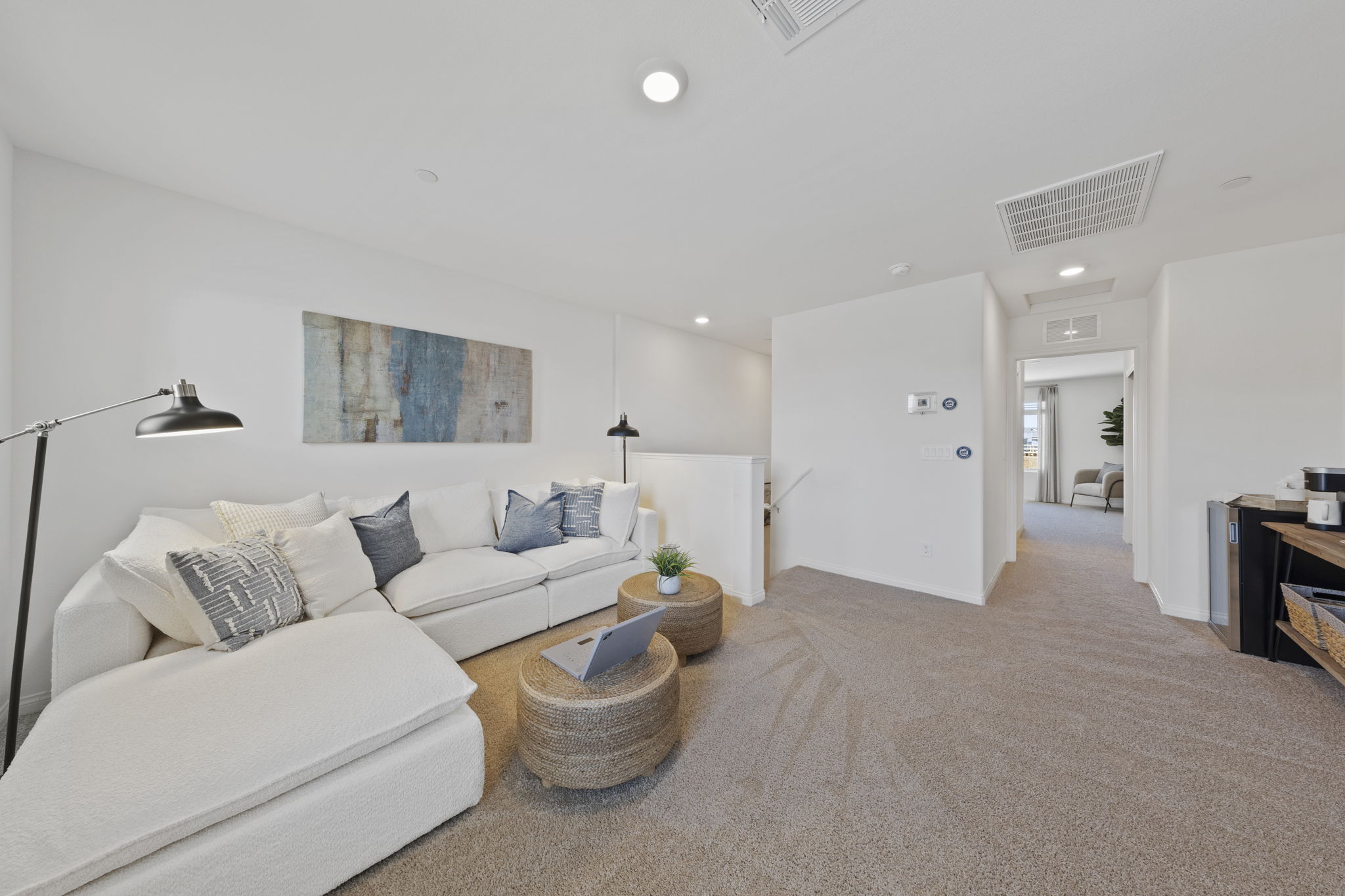 Cozy third-floor flow space featuring a white sectional sofa, woven coffee tables, and plush carpeting in a Solaris model home.