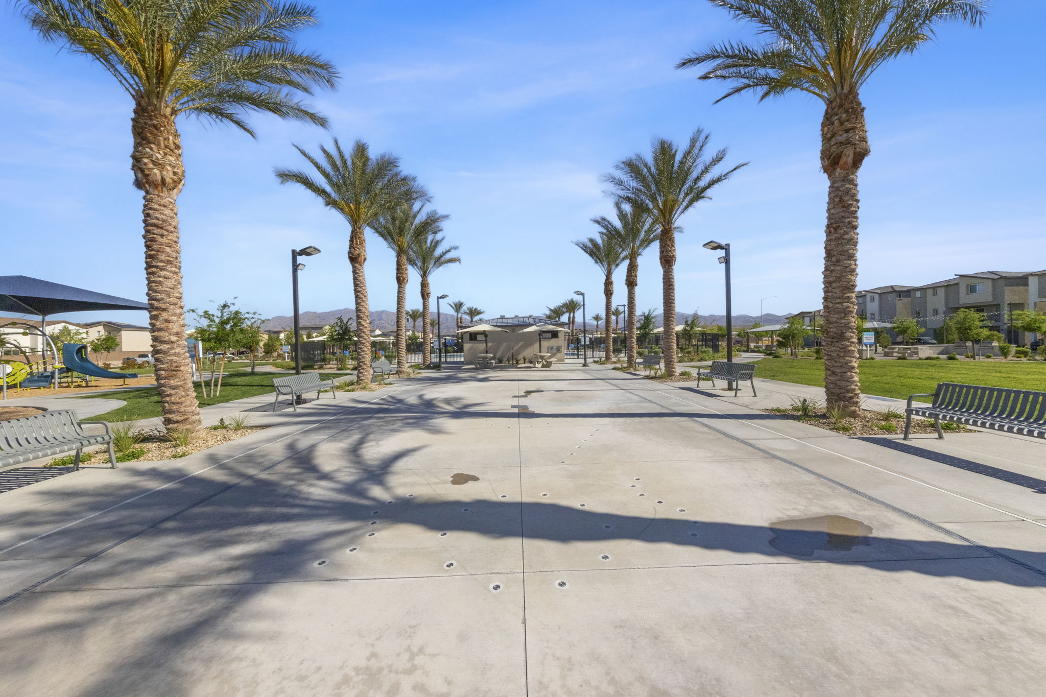 Paved splash pad area lined with tall palm trees and benches leading toward the central amenities at the Watercolor planned community.