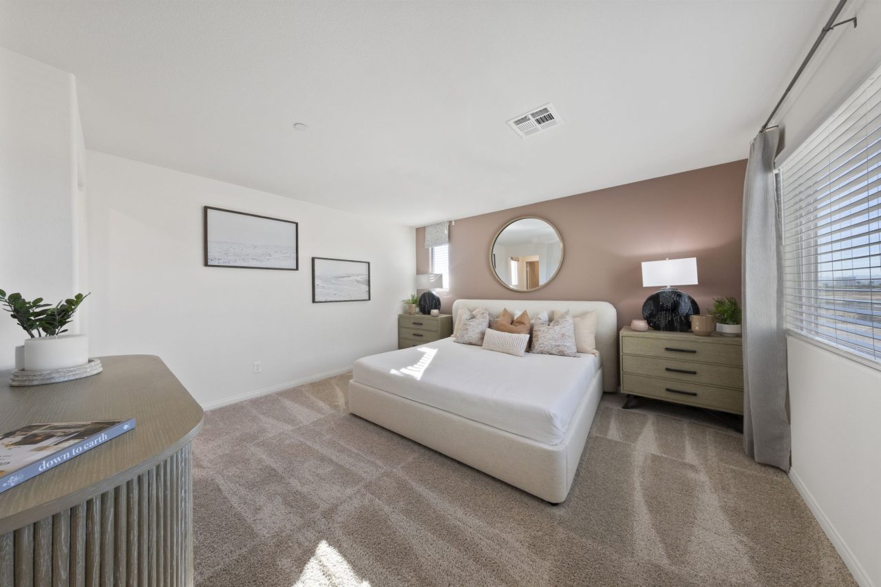 Spacious primary bedroom featuring a soft pink accent wall, a white upholstered bed, and modern furnishings in a Success model home.
