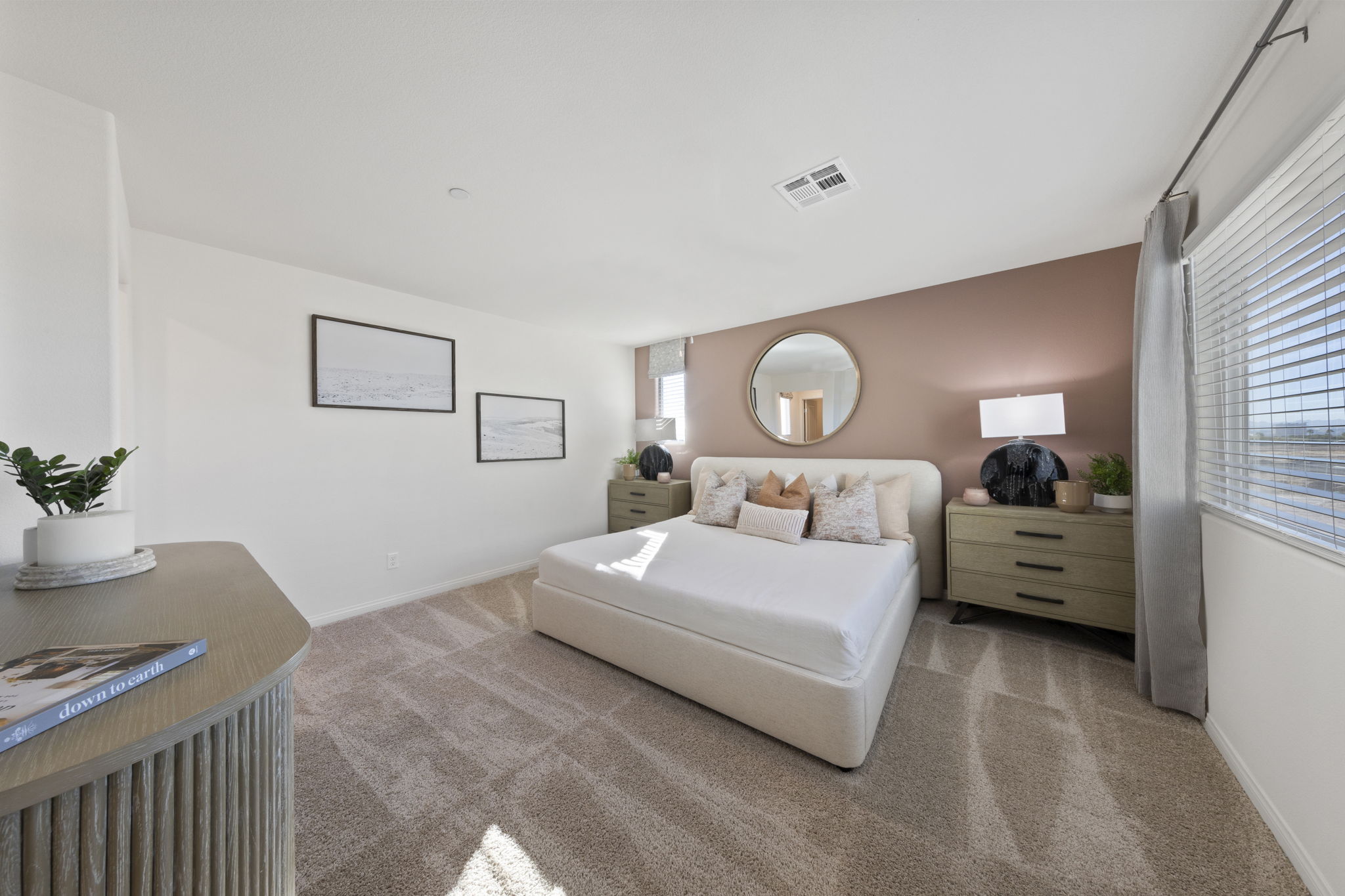 Spacious primary bedroom featuring a soft pink accent wall, a white upholstered bed, and modern furnishings in a Success model home.