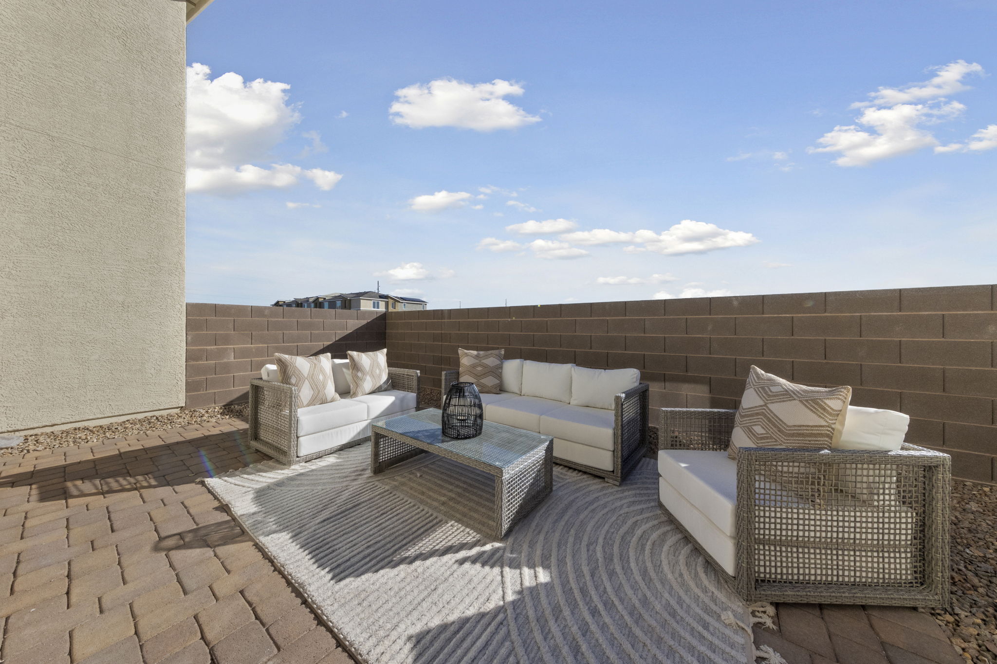 Private backyard patio space featuring brick pavers, a block wall enclosure, and comfortable patio seating under a blue sky.