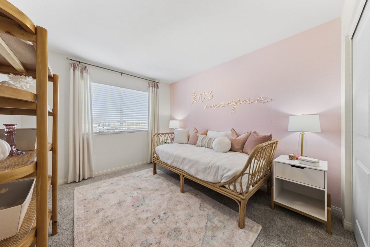 Charming secondary bedroom featuring a pink accent wall, a rattan daybed, and light-colored decor in a Touchstone Living home.