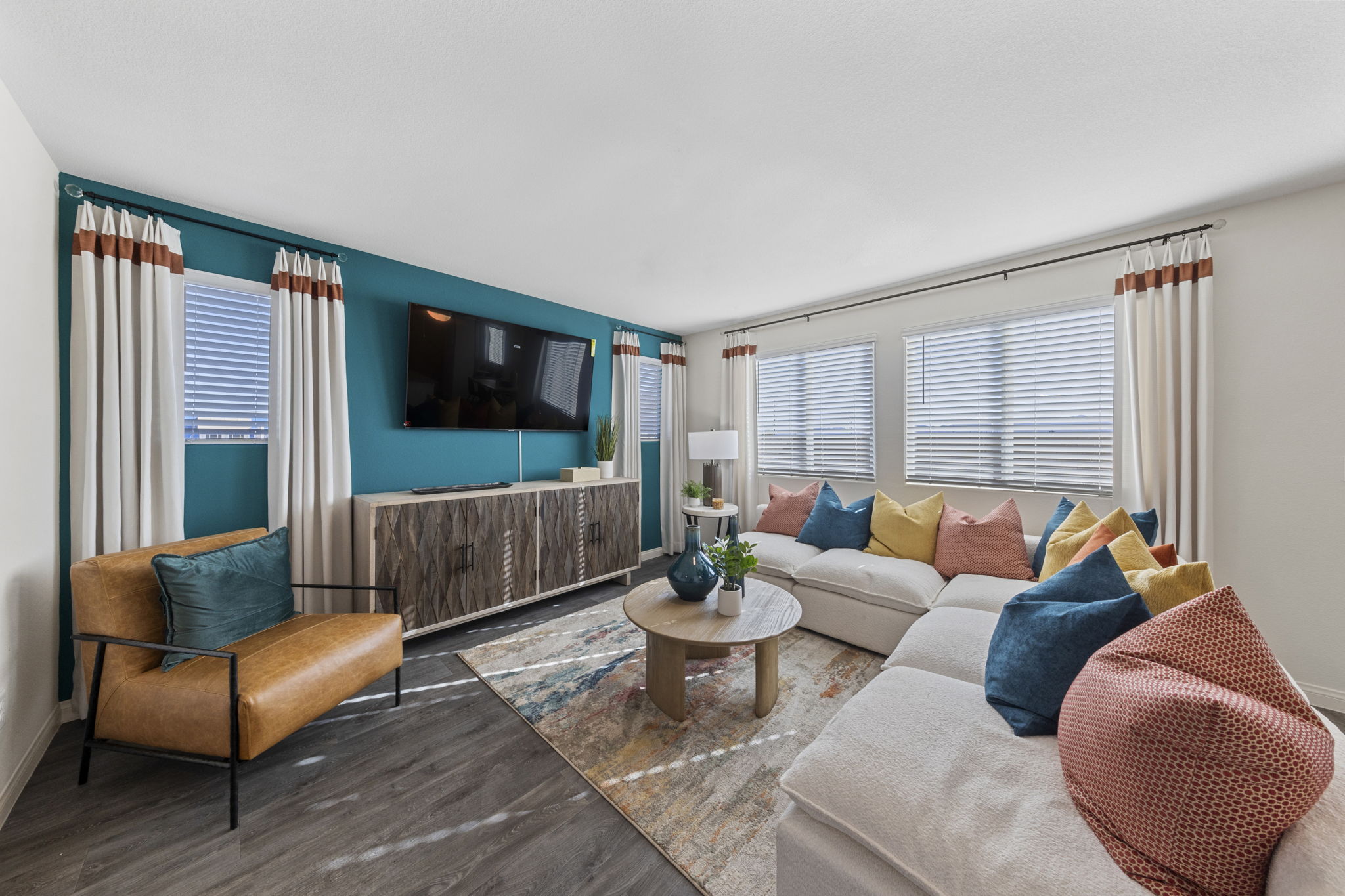 Stylish living room featuring a vibrant teal accent wall with a mounted TV, a large white sectional sofa, and a tan leather chair.