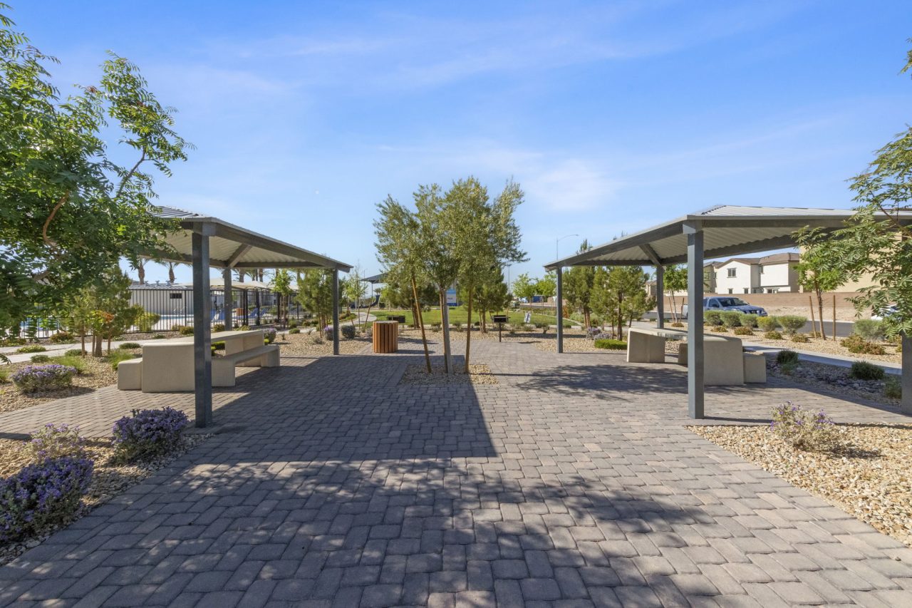 Two shaded picnic pavilions facing a wide paver walkway in a lushly landscaped park at the Watercolor planned community.