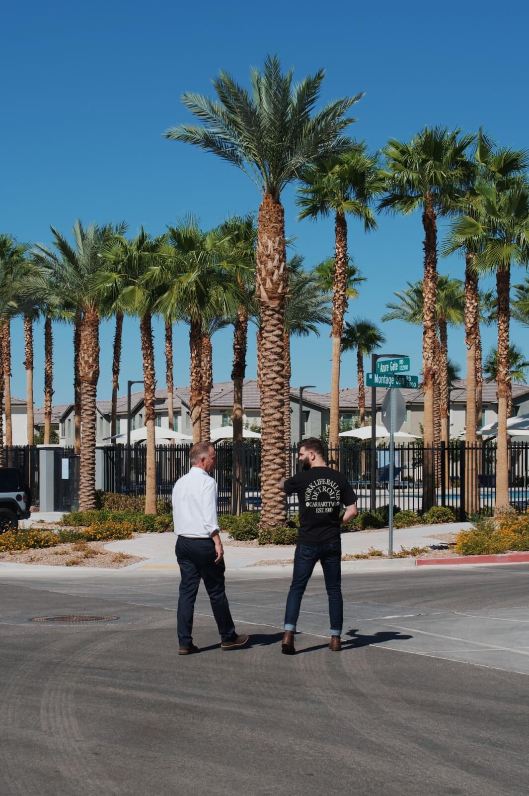 Two men standing outside near tall palm trees during a neighborhood tour at the Watercolor neighborhood in North Las Vegas.