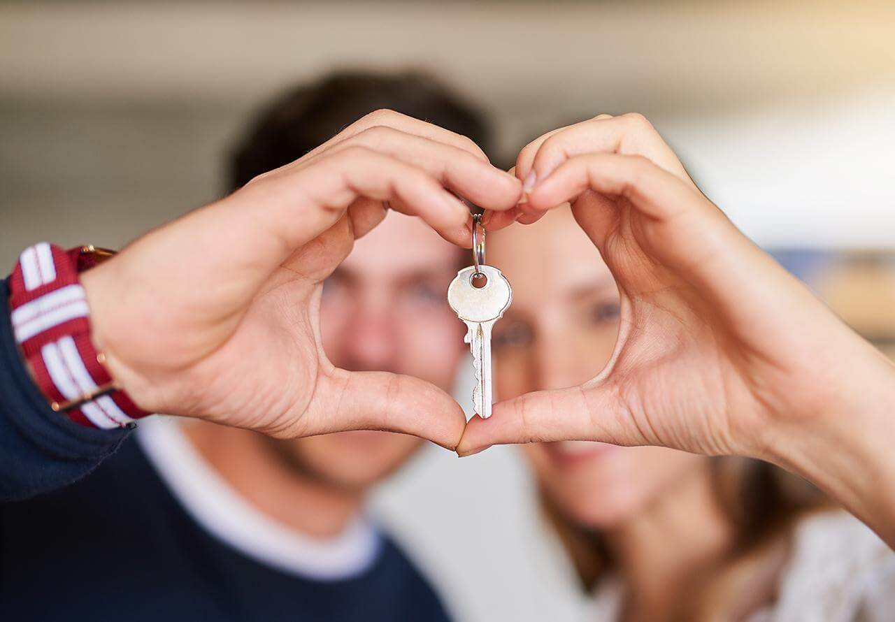 Close-up of a couple making a heart shape with their hands around a silver house key at a Touchstone Living neighborhood in Las Vegas.
