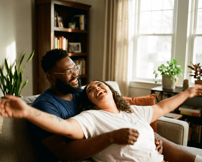 A happy young couple laughing and relaxing together on a living room couch inside a modern townhome at a Touchstone Living neighborhood.