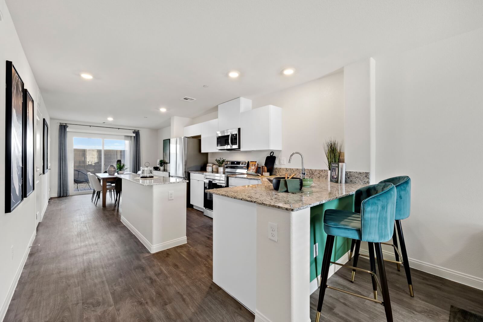 Modern open-concept kitchen featuring white cabinetry, granite countertops, and a peninsula bar with teal velvet stools in an Achieve 150 model home at the Independence neighborhood.