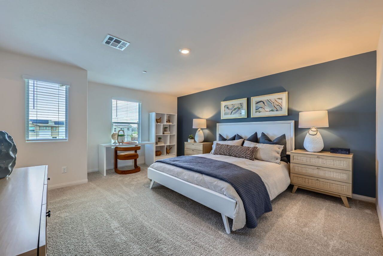 Spacious primary bedroom featuring a blue accent wall, white upholstered bed with blue bedding, and a built-in desk area in a Prosperity 280 model home at the Independence neighborhood.