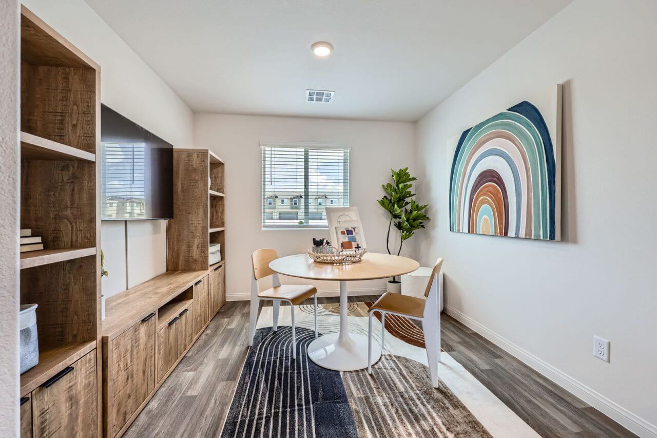 Versatile bonus room staged as a creative workspace with a round table, modern chairs, and built-in shelving in a Prosperity 300 home at the Independence neighborhood.