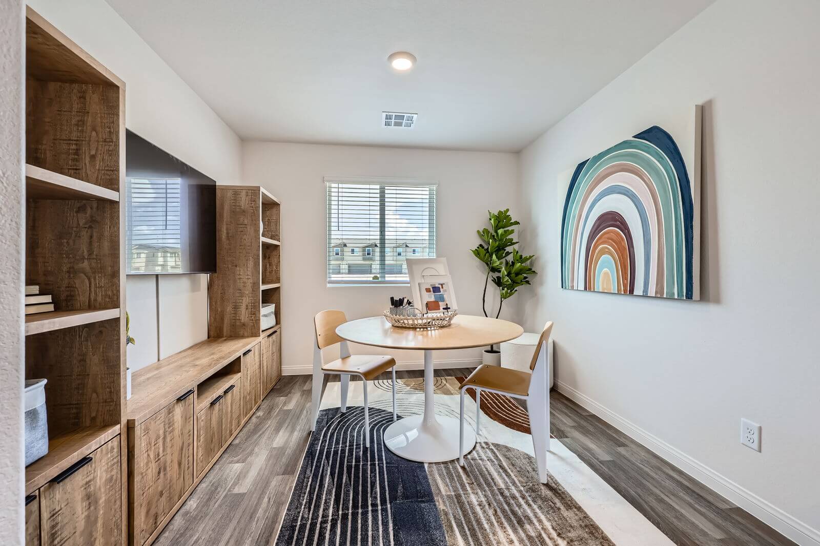 Versatile bonus room staged as a creative workspace with a round table, modern chairs, and built-in shelving in a Prosperity 300 home at the Independence neighborhood.