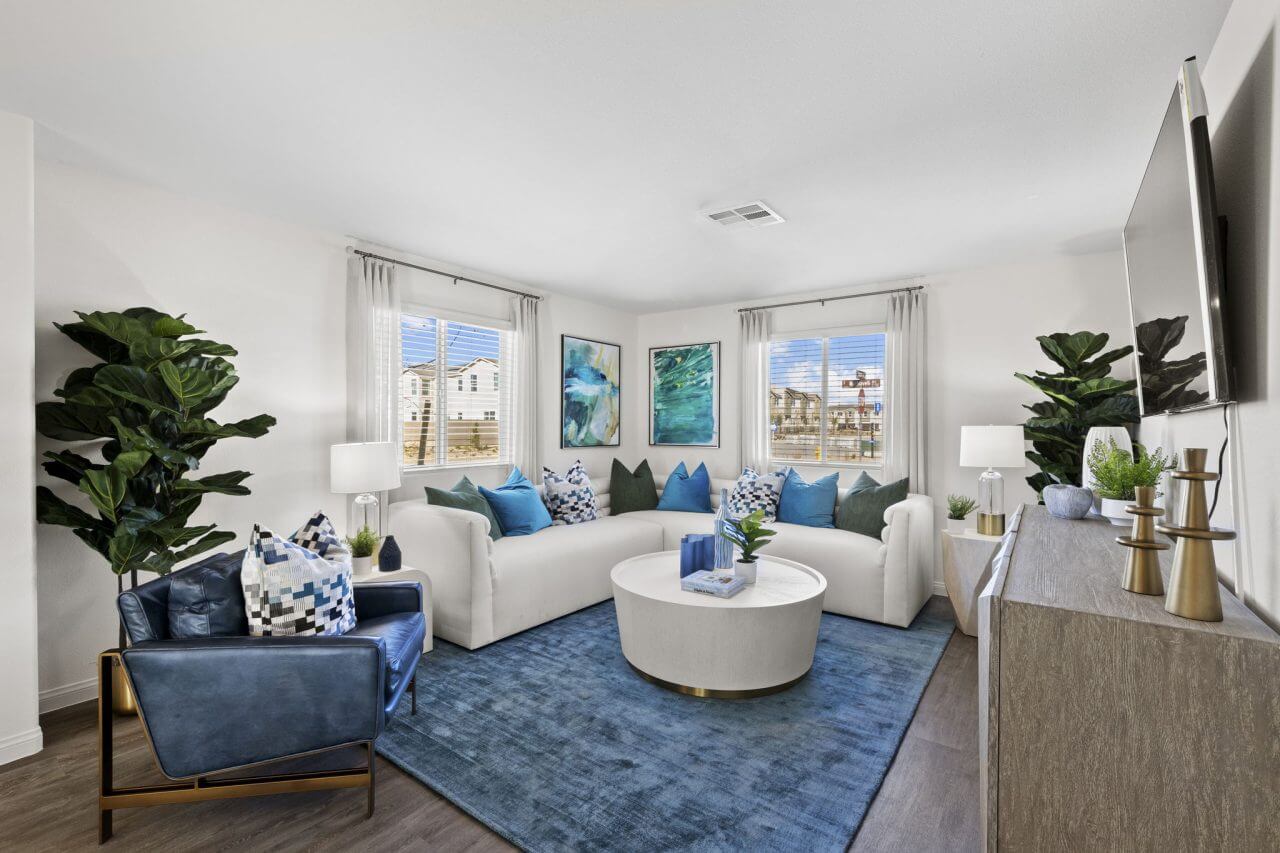 Bright, open-concept living room featuring a white sectional sofa, a blue leather armchair, and a blue area rug in a Success 160 home at the Independence neighborhood.