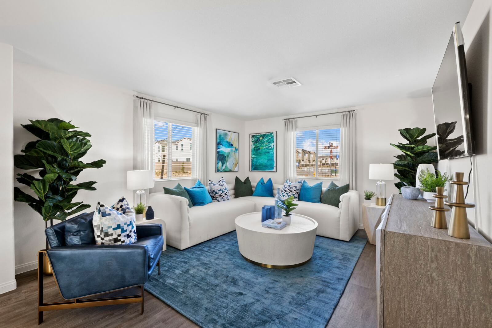 Bright, open-concept living room featuring a white sectional sofa, a blue leather armchair, and a blue area rug in a Success 160 home at the Independence neighborhood.