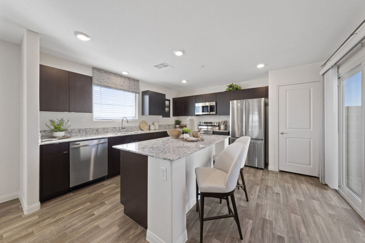 Modern kitchen featuring dark wood cabinetry, granite countertops, a center island with seating, and upgraded vinyl flooring in a Success 180 home at the Independence neighborhood.