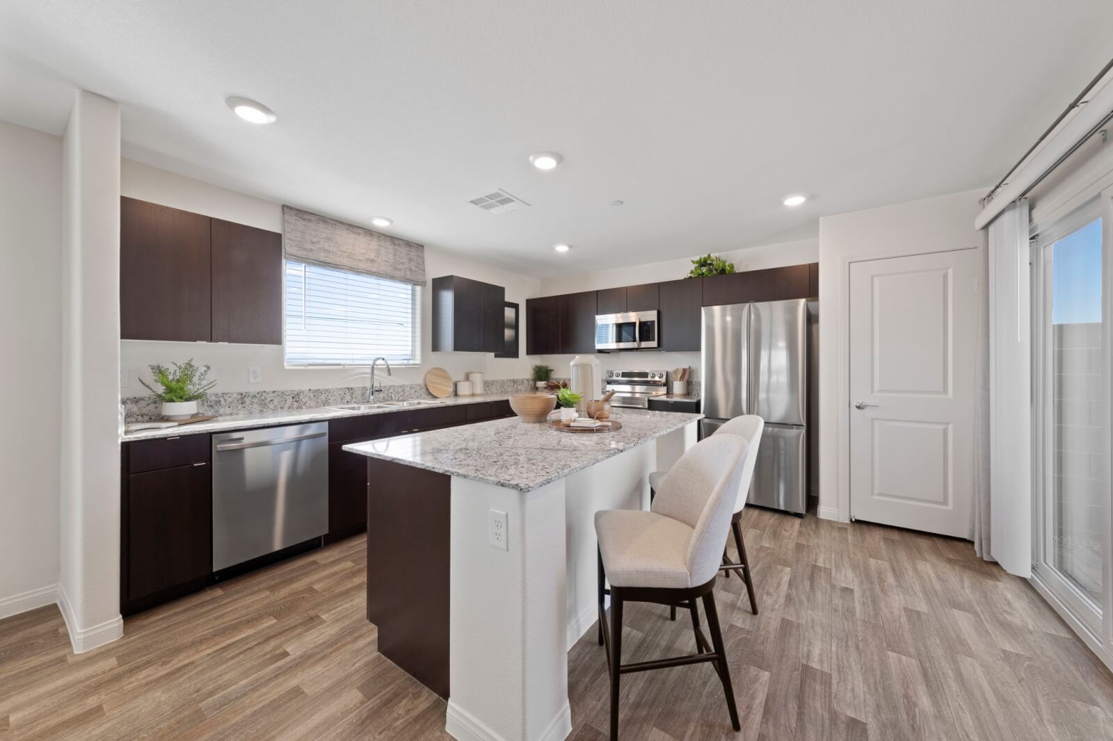 Modern kitchen featuring dark wood cabinetry, granite countertops, a center island with seating, and upgraded vinyl flooring in a Success 180 home at the Independence neighborhood.