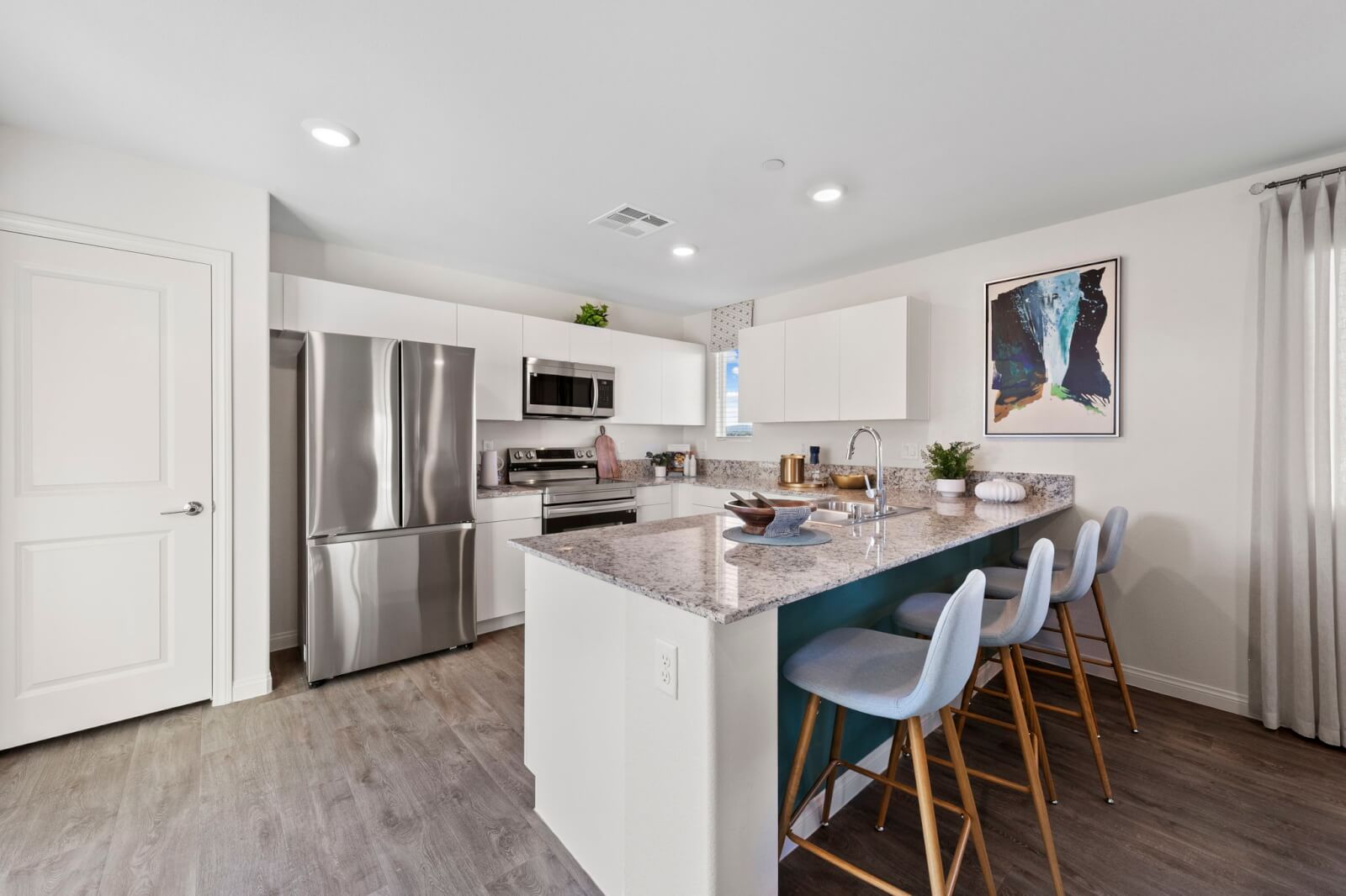 Modern open-concept kitchen featuring white cabinetry, granite countertops, upgraded vinyl flooring, and a peninsula with blue barstools in a Success 180 home at the Independence neighborhood.