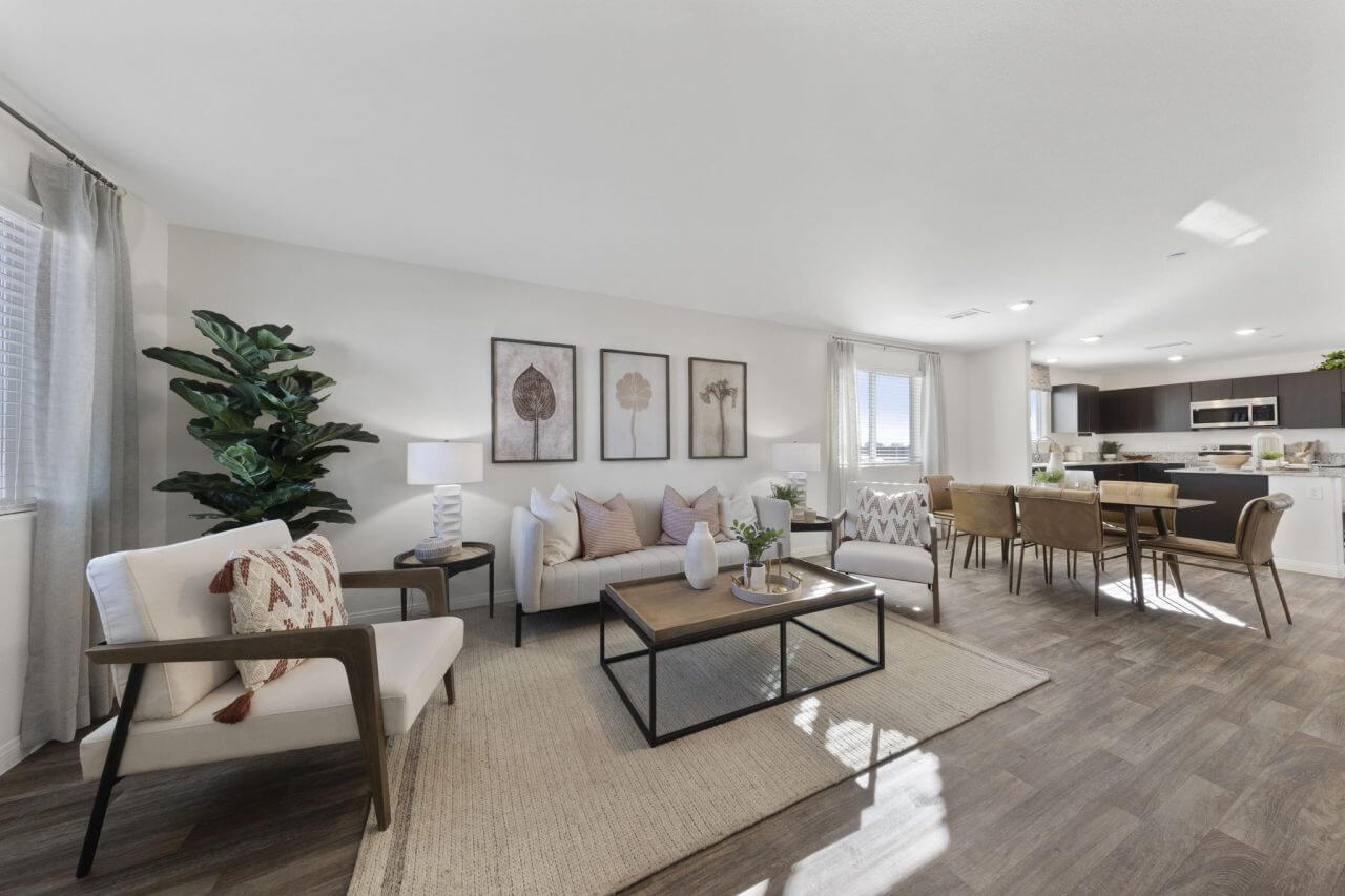 Expansive open-concept living and dining area featuring a light beige sofa, accent chairs, and a large jute rug in a Success 180 home at the Independence neighborhood.