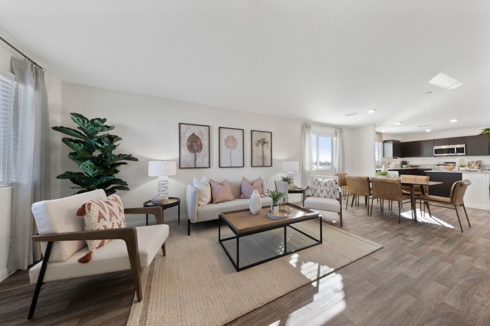 Expansive open-concept living and dining area featuring a light beige sofa, accent chairs, and a large jute rug in a Success 180 home at the Independence neighborhood.