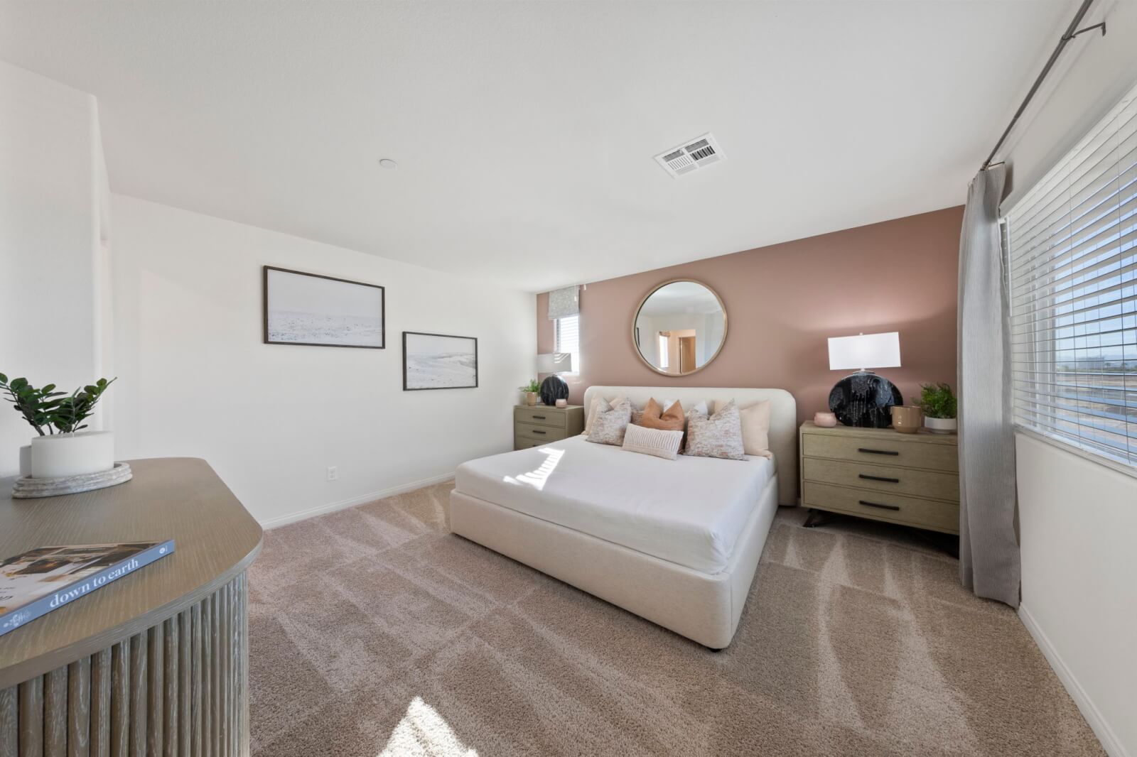 Spacious primary bedroom featuring a soft pink accent wall, a white upholstered bed, and modern furnishings in a Success 180 home at the Independence neighborhood.