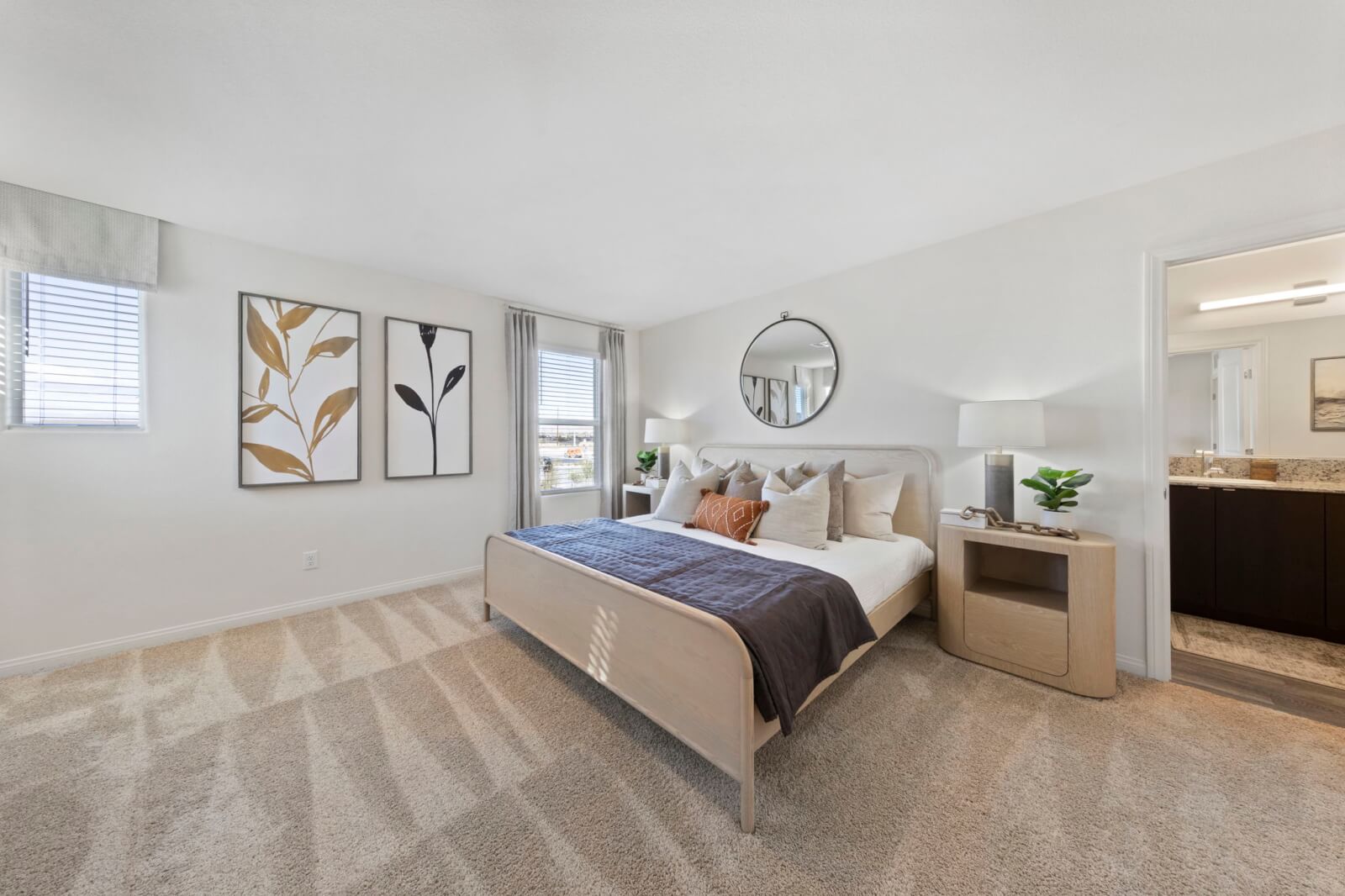 Spacious primary bedroom featuring a light wood bed, plush carpeting, and an attached en-suite bathroom in a Triumph 240 home at the Independence neighborhood.