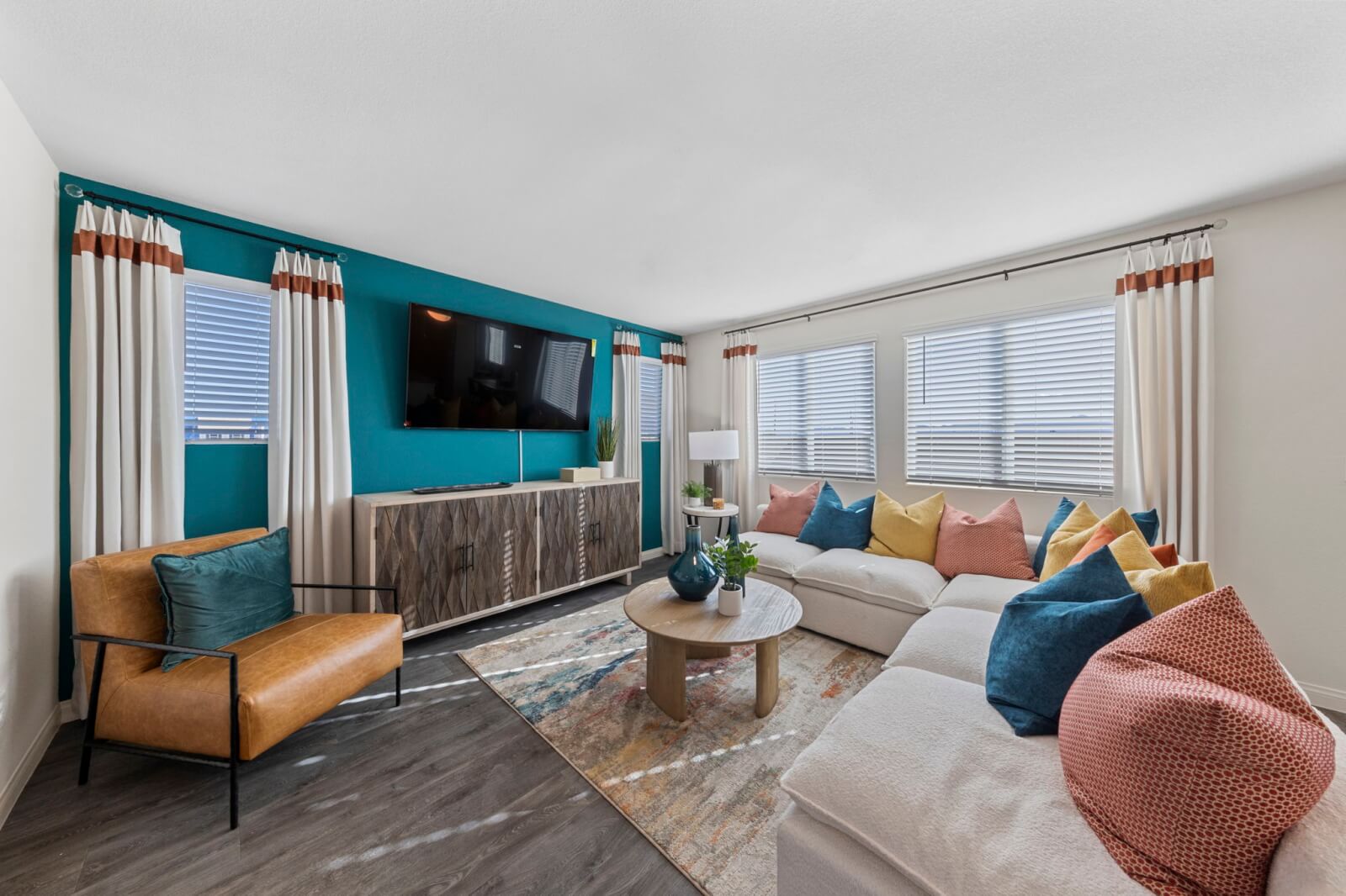 Stylish living room featuring a vibrant teal accent wall with a mounted TV, a large white sectional sofa, and a tan leather chair in a Triumph 250 home at the Independence neighborhood.