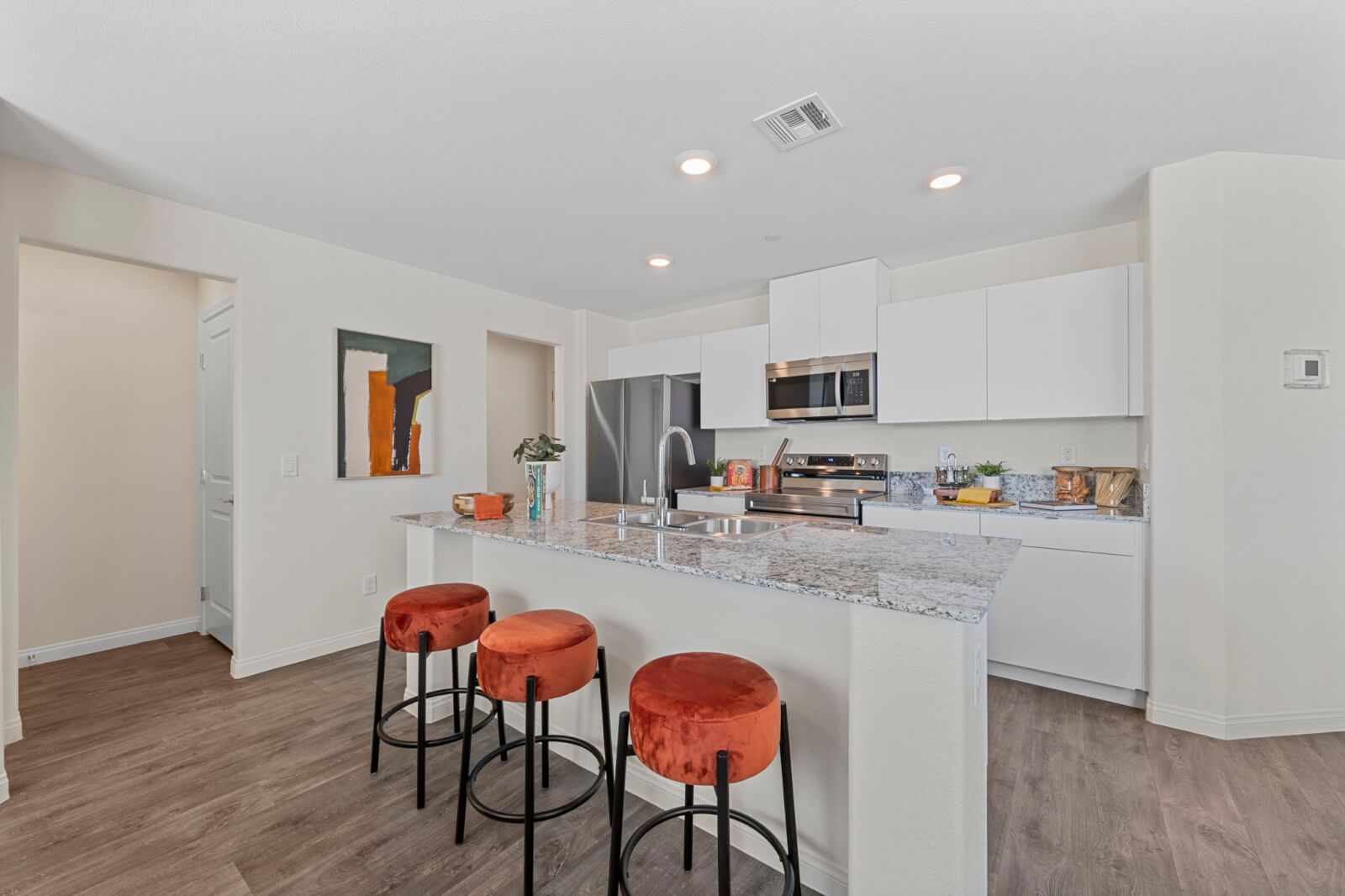 Open-concept kitchen with white cabinetry, stainless steel Samsung® appliances, and a granite island with three orange barstools at the Independence neighborhood.