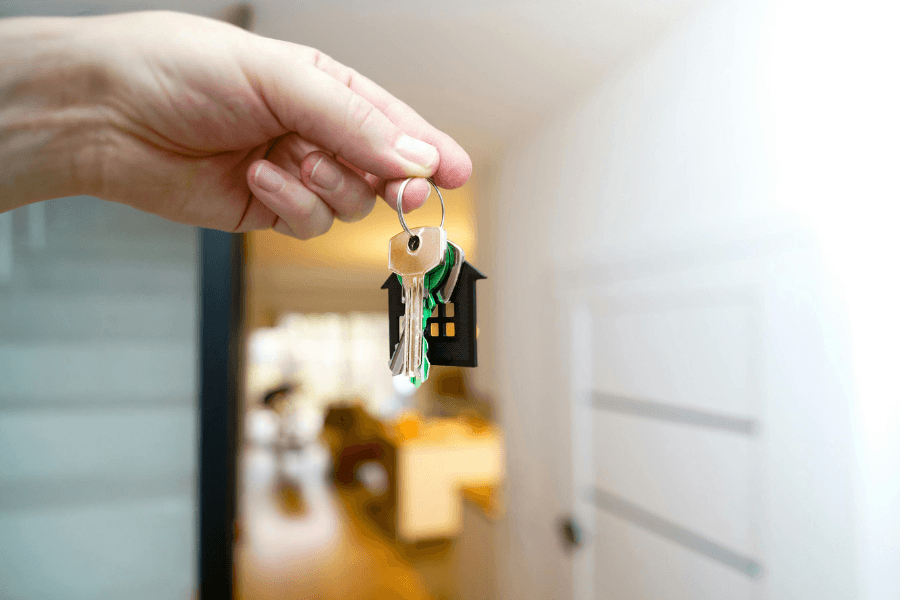 Close-up of a new homeowner holding a silver key with a house-shaped keychain at a Touchstone Living neighborhood in Las Vegas.