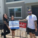 A happy family celebrates purchasing their new Las Vegas townhome, smiling and holding up closing signs outside their property at a Touchstone Living neighborhood.