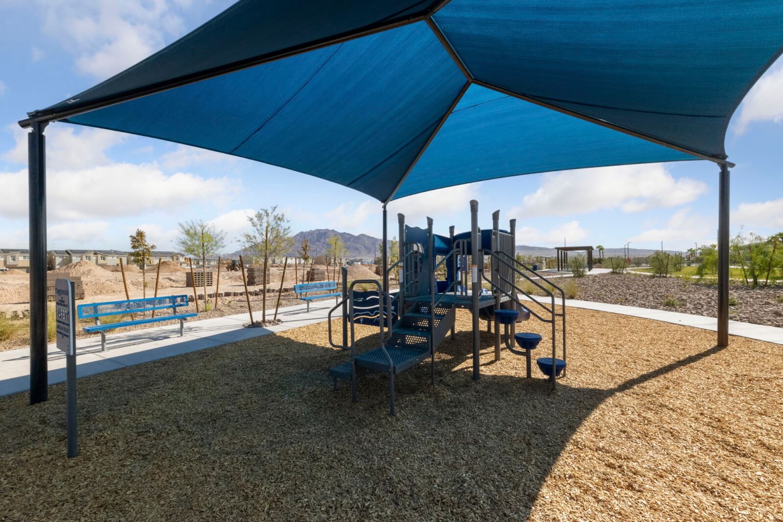 Modern children’s playground featuring climbing structures and a large blue shade structure on a bark surface at the Independence planned neighborhood.