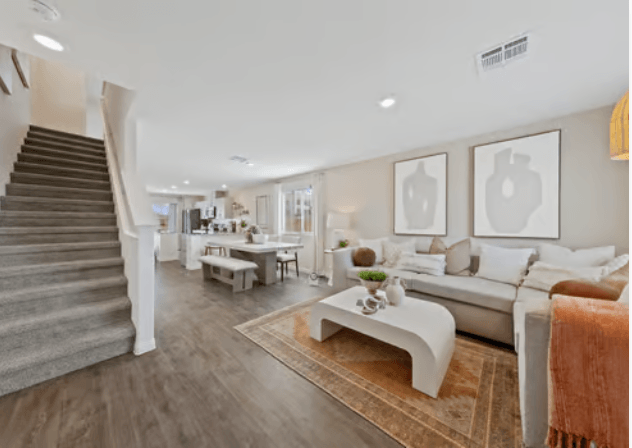 Open-concept living room and dining area featuring upgraded vinyl flooring, a light beige sectional sofa, and carpeted stairs in plans 100 & 130 at Solaris.