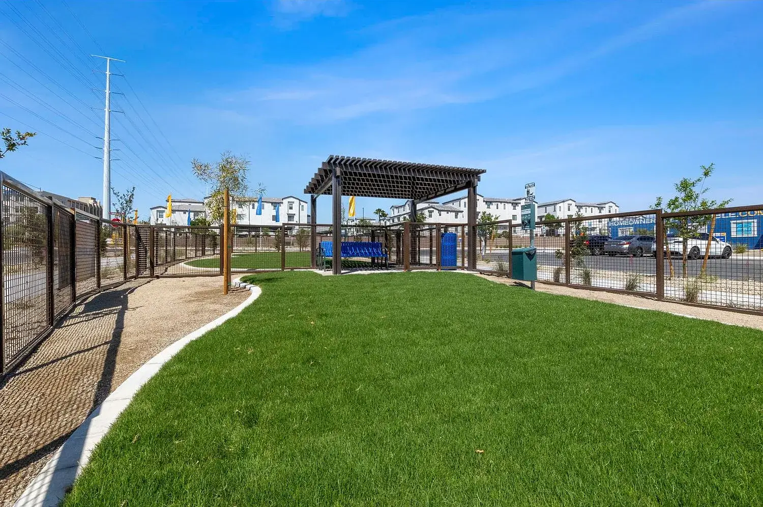 Fenced-in community dog park featuring green turf, a walking path, and a shaded seating area at the Solaris at Russell neighborhood.
