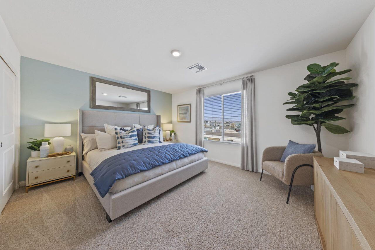 Spacious primary bedroom featuring a light blue accent wall, a large bed with blue bedding, and a large mirror in a Solaris Las Vegas new build townhome model at the Solaris at Warm Springs neighborhood.