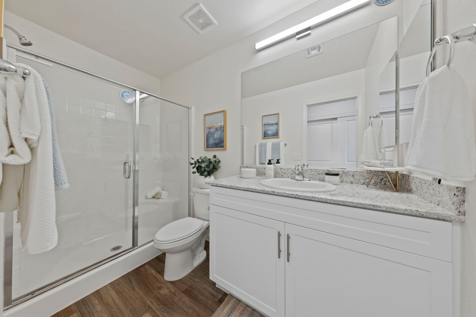 Modern full bathroom featuring a white vanity with granite countertops, a glass-enclosed shower, and upgraded vinyl flooring at the Solaris at Warm Springs neighborhood.