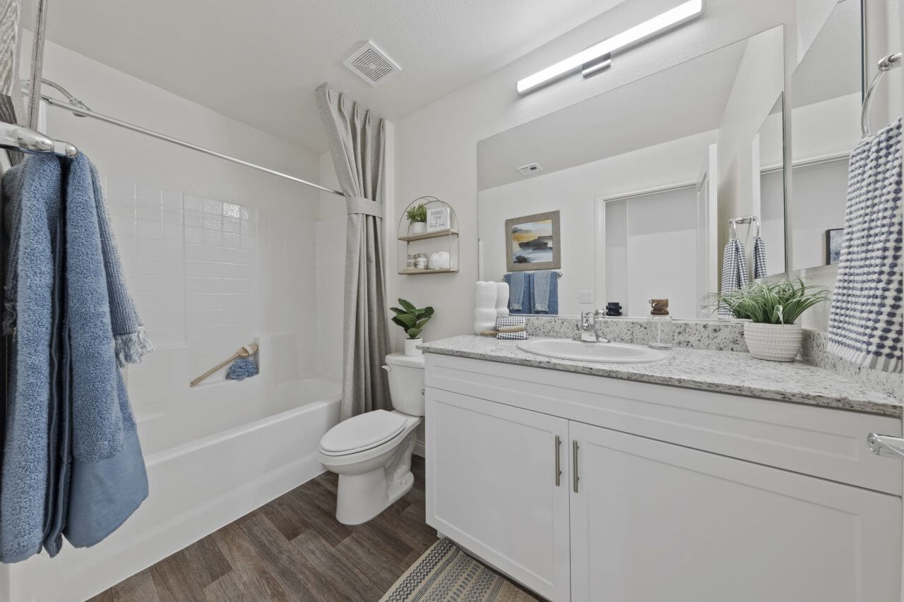 Modern bathroom featuring a white vanity with granite countertops, upgraded vinyl flooring, and a shower and tub combination at the Solaris at Warm Springs neighborhood.
