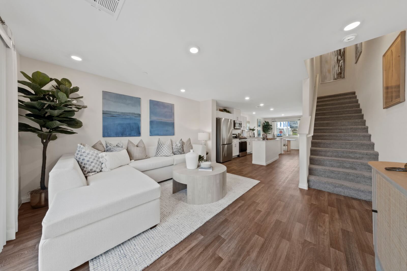 Expansive open-concept living room and kitchen featuring upgraded vinyl flooring, a white sectional, and stainless steel Samsung® appliances at the Solaris at Warm Springs neighborhood.