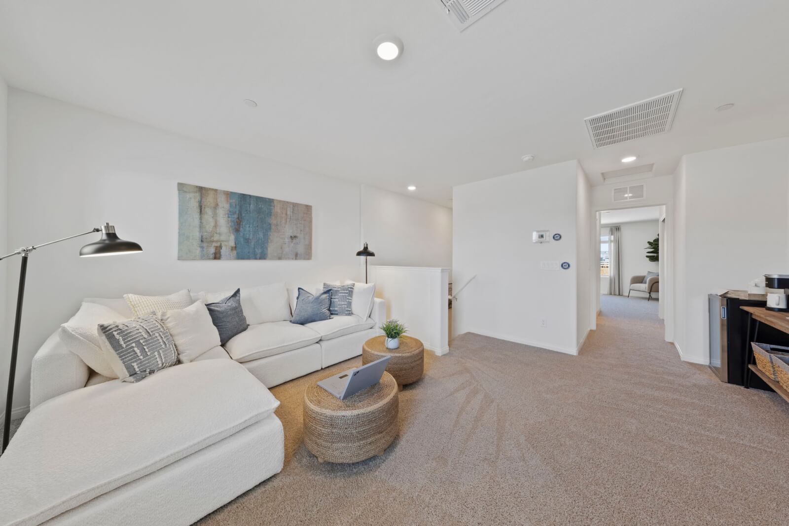 Cozy third-floor flow space featuring a white sectional sofa, woven coffee tables, and plush carpeting in a Solaris model at the Solaris at Warm Springs neighborhood.