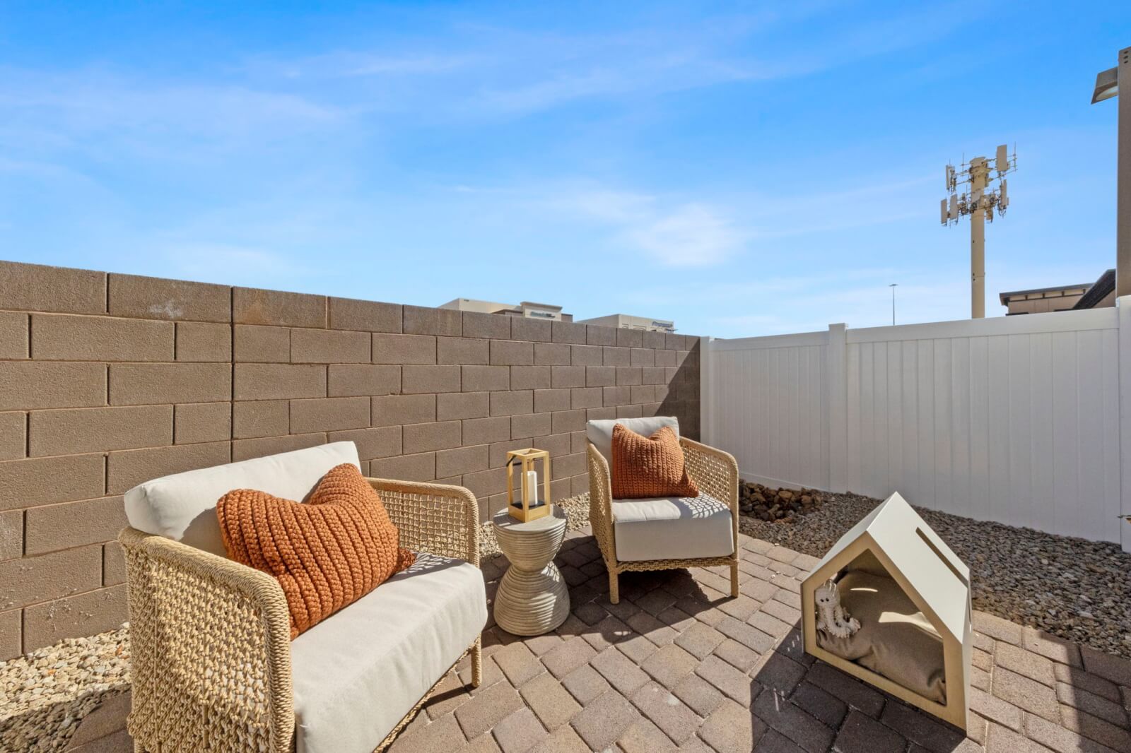 Private enclosed backyard patio featuring brick pavers, modern woven chairs with orange pillows, and a small dog house at the Solaris at Warm Springs neighborhood.