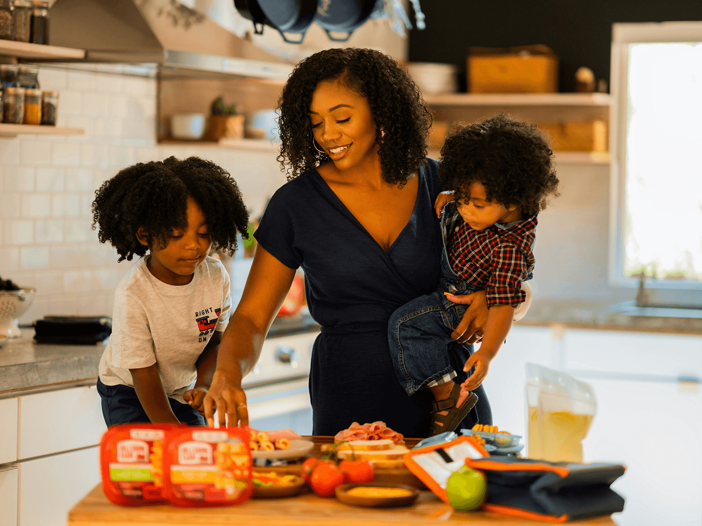 A smiling mother preparing lunch for her two young children at a spacious island in a modern townhome kitchen within a Touchstone Living neighborhood.
